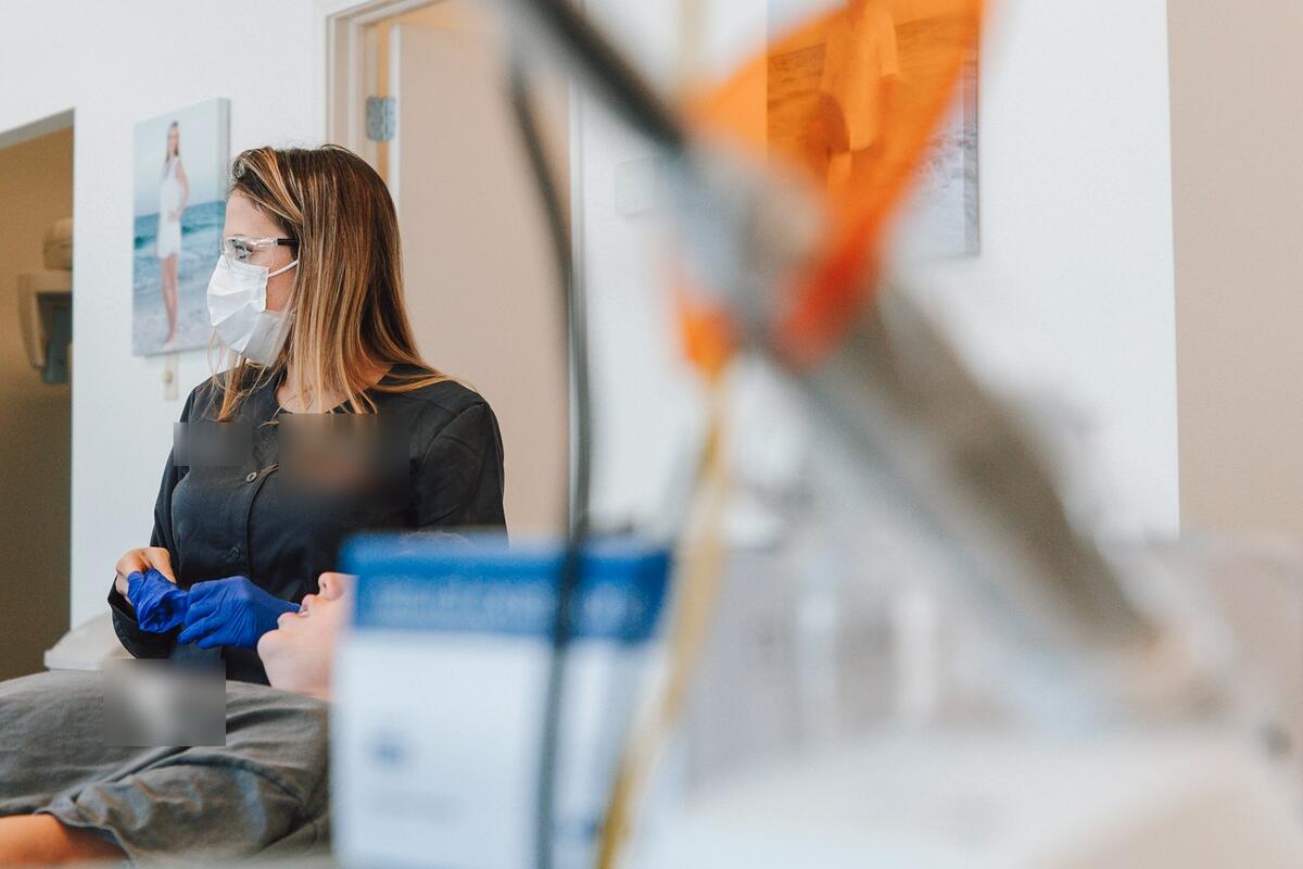 A hygienist pulling on gloves beside a patient resting in the chair