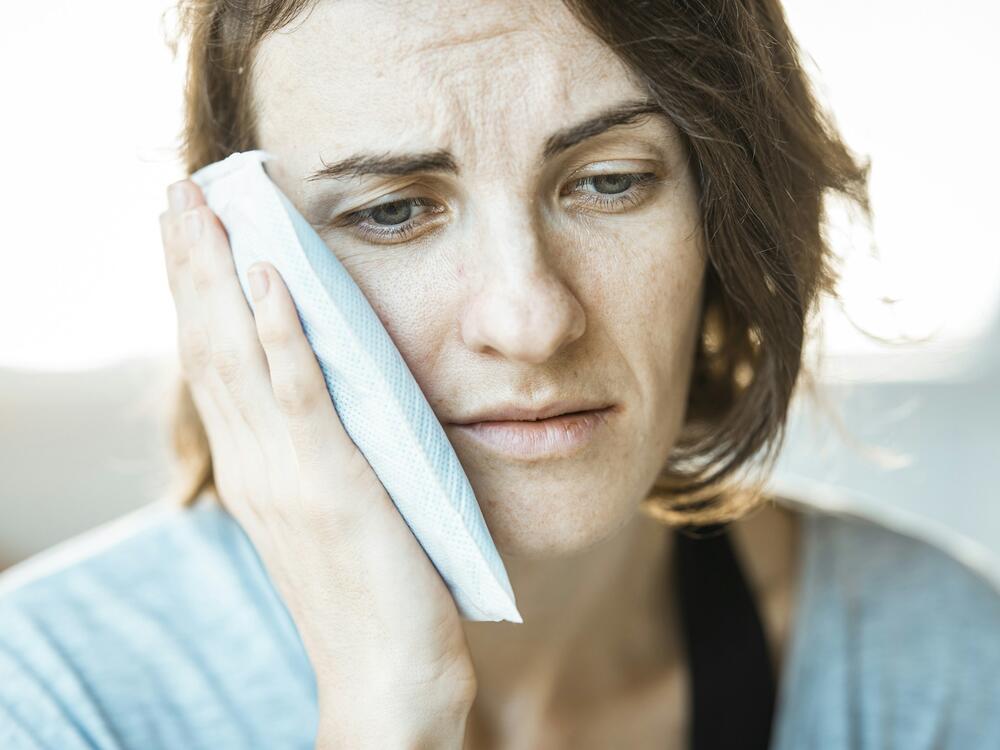 A woman holding a cold compress to her aching cheek