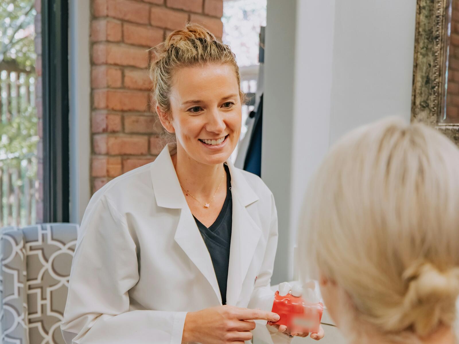 Dr. Brennan, smiling, shows a patient a model of a crown in a bright consult room