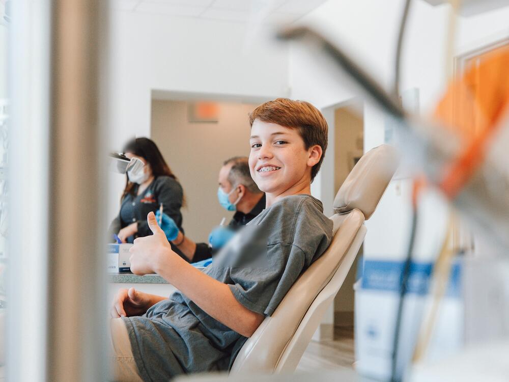 A boy with braces giving a thumbs-up from the dental chair
