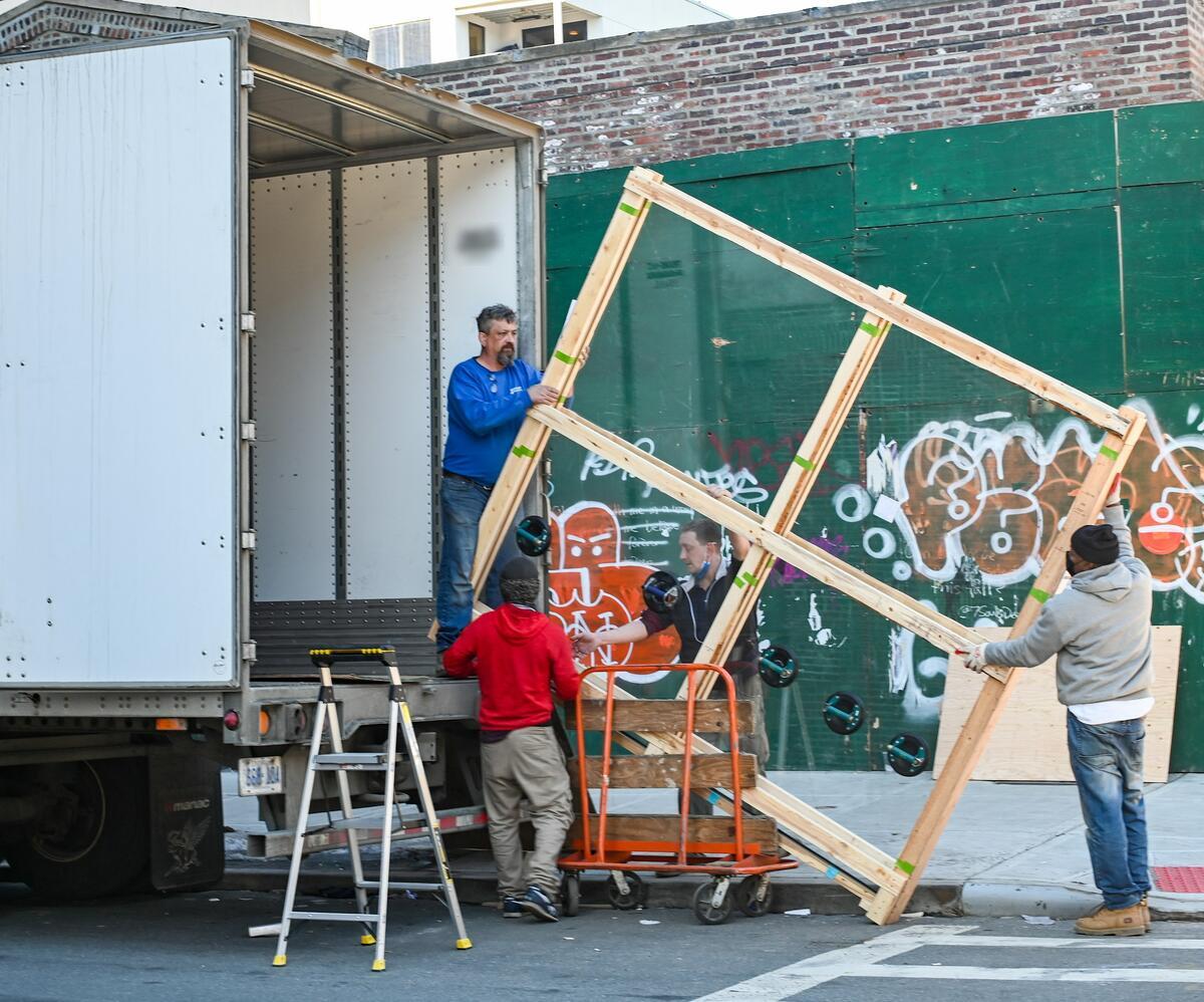 A four-person crew loading a large crate into the back of a white box truck