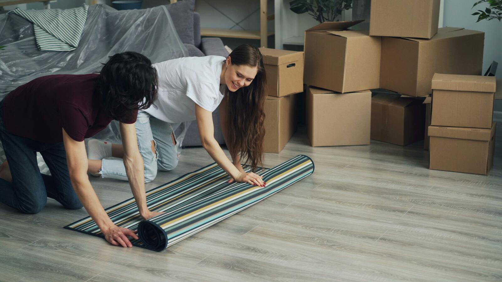 A couple rolling out a rug among stacked moving boxes in their new home
