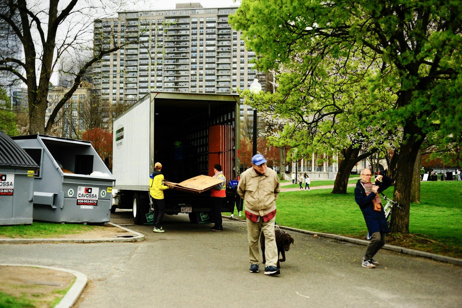 Movers unloading furniture from the back of a box truck parked beside a park