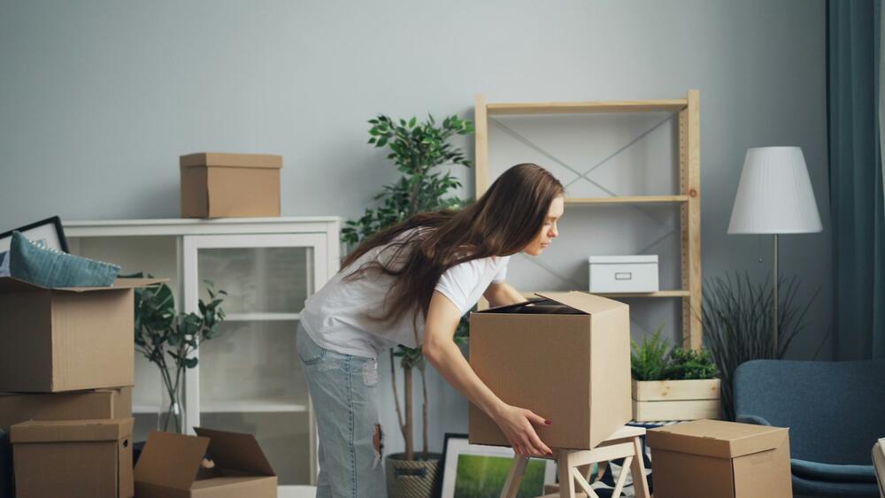 A woman packing cardboard boxes in a bright living room