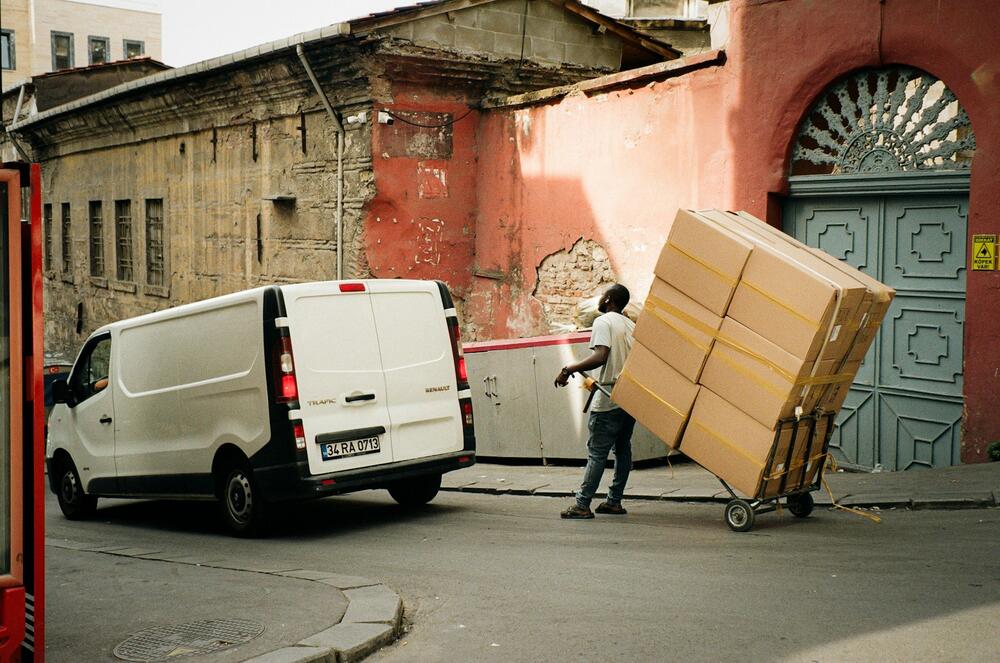 A mover wheeling a stack of boxes on a dolly toward a white van