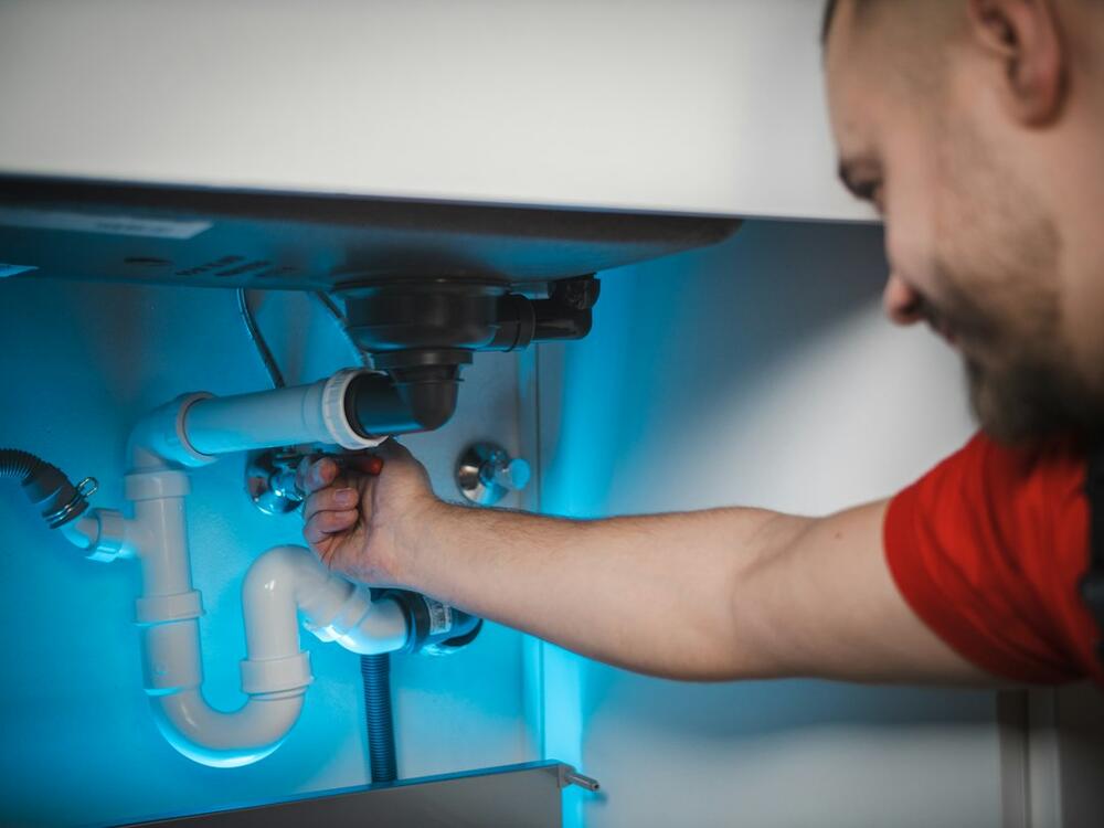 A plumber reaching under a bathroom sink to work on the trap and drain pipes